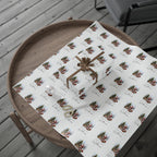 A gift box wrapped in white wrapping paper with a repeating Christmas tree, Santa Claus and Reindeer pattern with the text 'Merry Christmas William', tied with a brown ribbon, displayed on a round wooden tray over a grey deck floor.