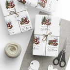 Three gift wrapped packages tied with twine on a light surface, featuring a Christmas print with Santa, trees, reindeer, and the text 'Merry Christmas William.' A ball of twine, scissors, and round tags are arranged around them.