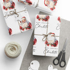Personalised Christmas wrapping paper featuring classic watercolour Santa Claus design with the name Charlotte, wrapped gifts, twine, gift tags and scissors.