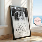 A framed personalised wedding photo print leaning against a window on a wooden floor. The black frame contains a black and white photo of a couple with the names 'RYAN & CHELSEA' and 'MONTGOMERY' printed in large black text, along with wedding date details.