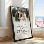 A framed personalised wedding print leaning against a window on a wooden floor. The black framed poster shows a couple at the top and large text reading 'RYAN & CHELSEA' with 'MONTGOMERY' below, plus wedding date details.