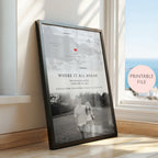 A framed personalised map and photo print leaning against a window on a wooden floor. The print includes a black and white map with a red heart marking, and a black and white couple photograph.